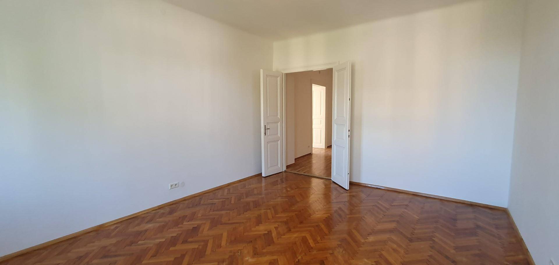 Helles Schlafzimmer mit Fischgrätparkett und einer Doppeltür, die in einen weiteren Raum führt.