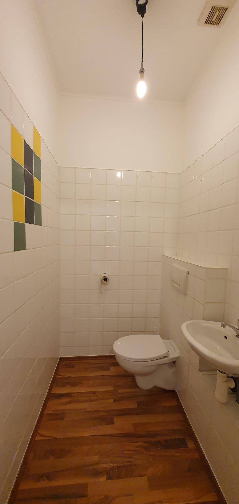 Separate Toilette mit Waschbecken und farbigen Akzentfliesen an der Wand.