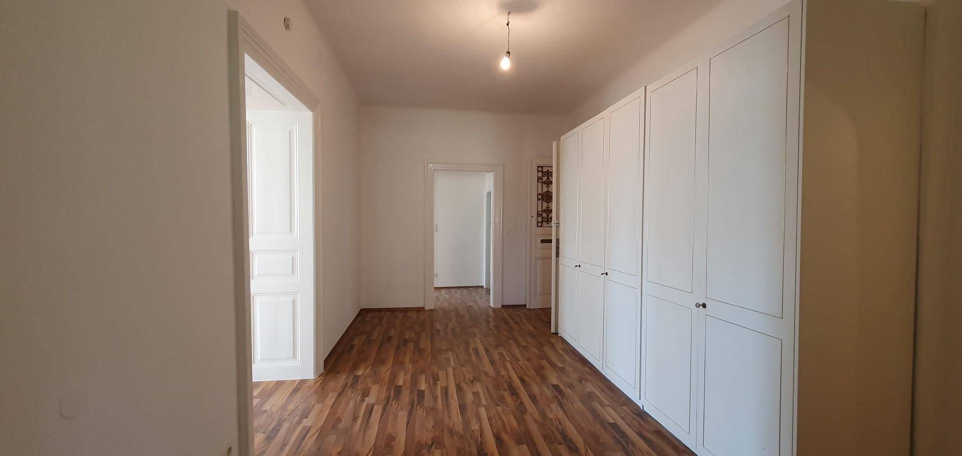 Heller Flur mit Holzboden und einer Reihe von weißen Einbauschränken für Stauraum.