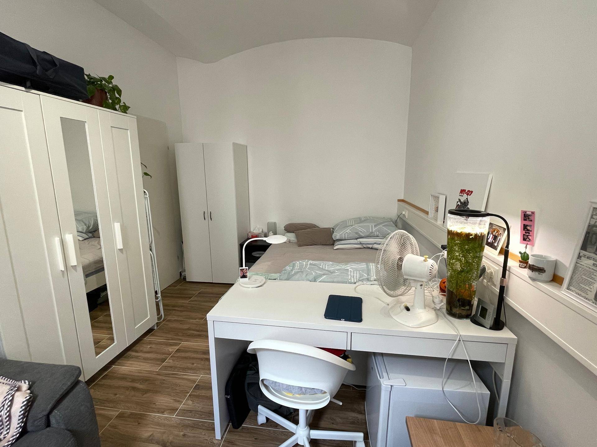 Schlafzimmer mit Bett, Schreibtisch und Kleiderschränken, hell beleuchtet durch natürliches Licht.