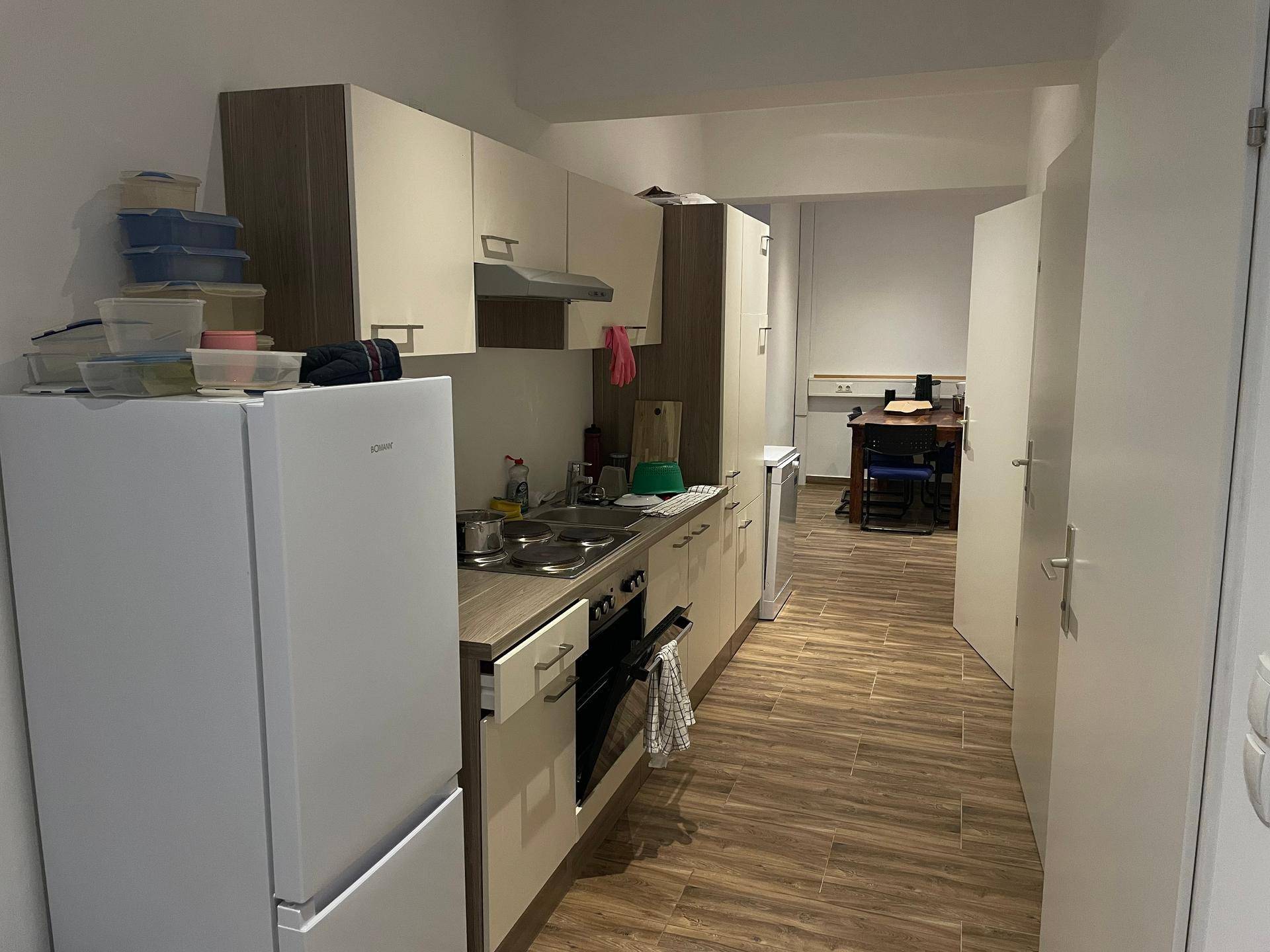 Funktionale Küche mit Einbaugeräten, Kühlschrank und Holzoptik-Arbeitsplatte, führt in einen weiteren Raum.