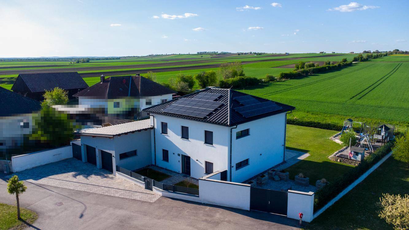 Luftaufnahme des modernen Hauses von vorne, umgeben von weiten Feldern und Grünflächen.