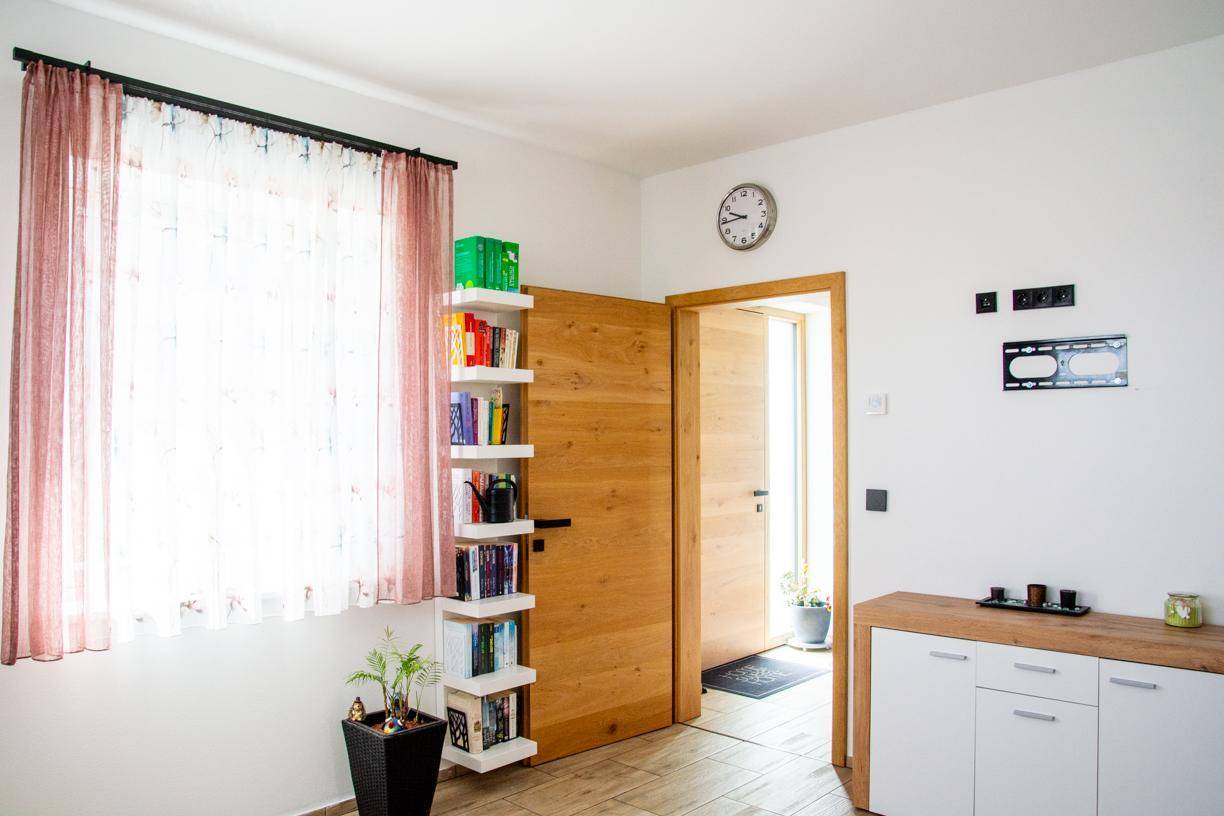Helles Schlafzimmer mit Fenster, Bücherregal und Holztüren.