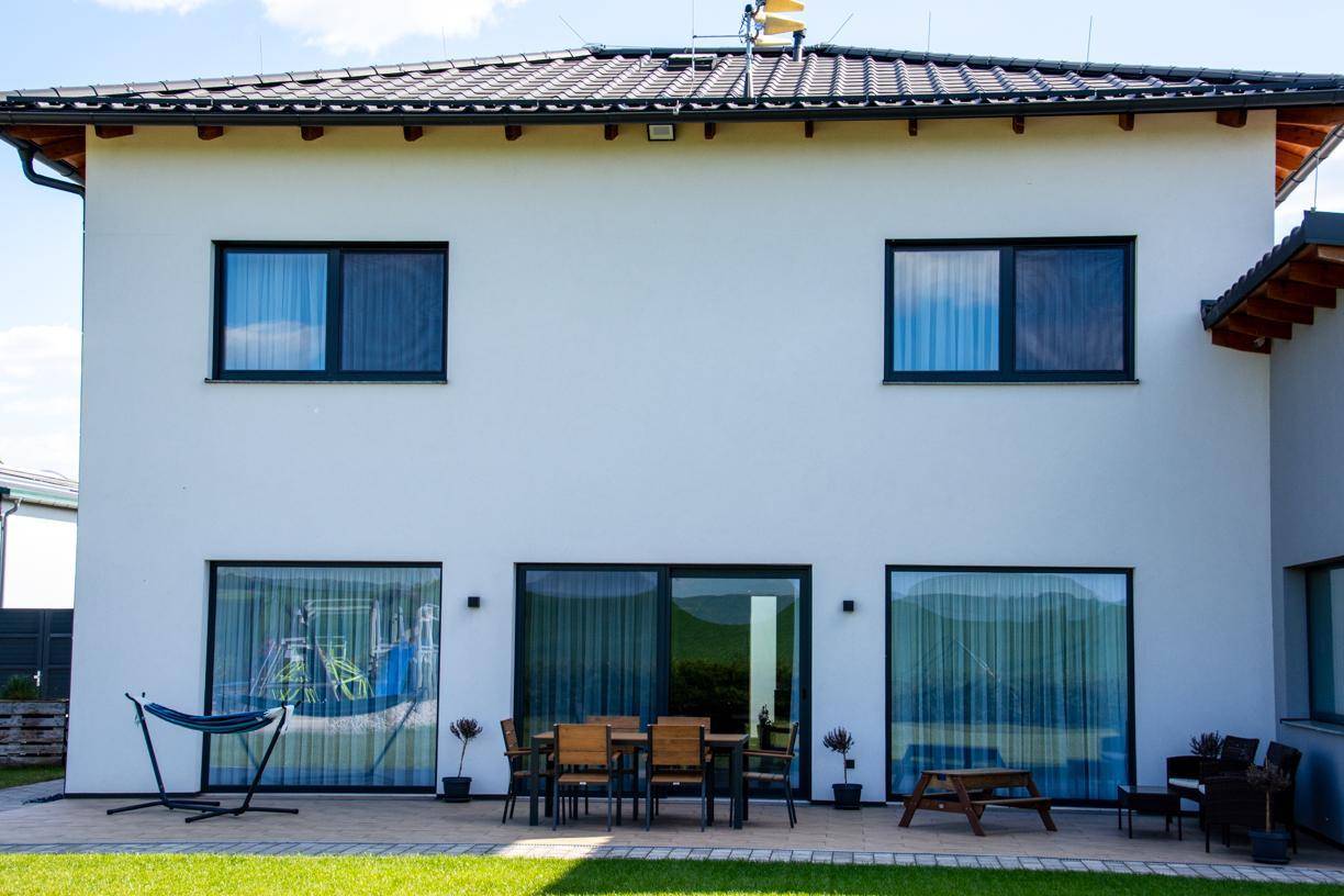 Rückansicht des Hauses mit großer Terrasse, bodentiefen Fenstern und einer entspannenden Hängematte.