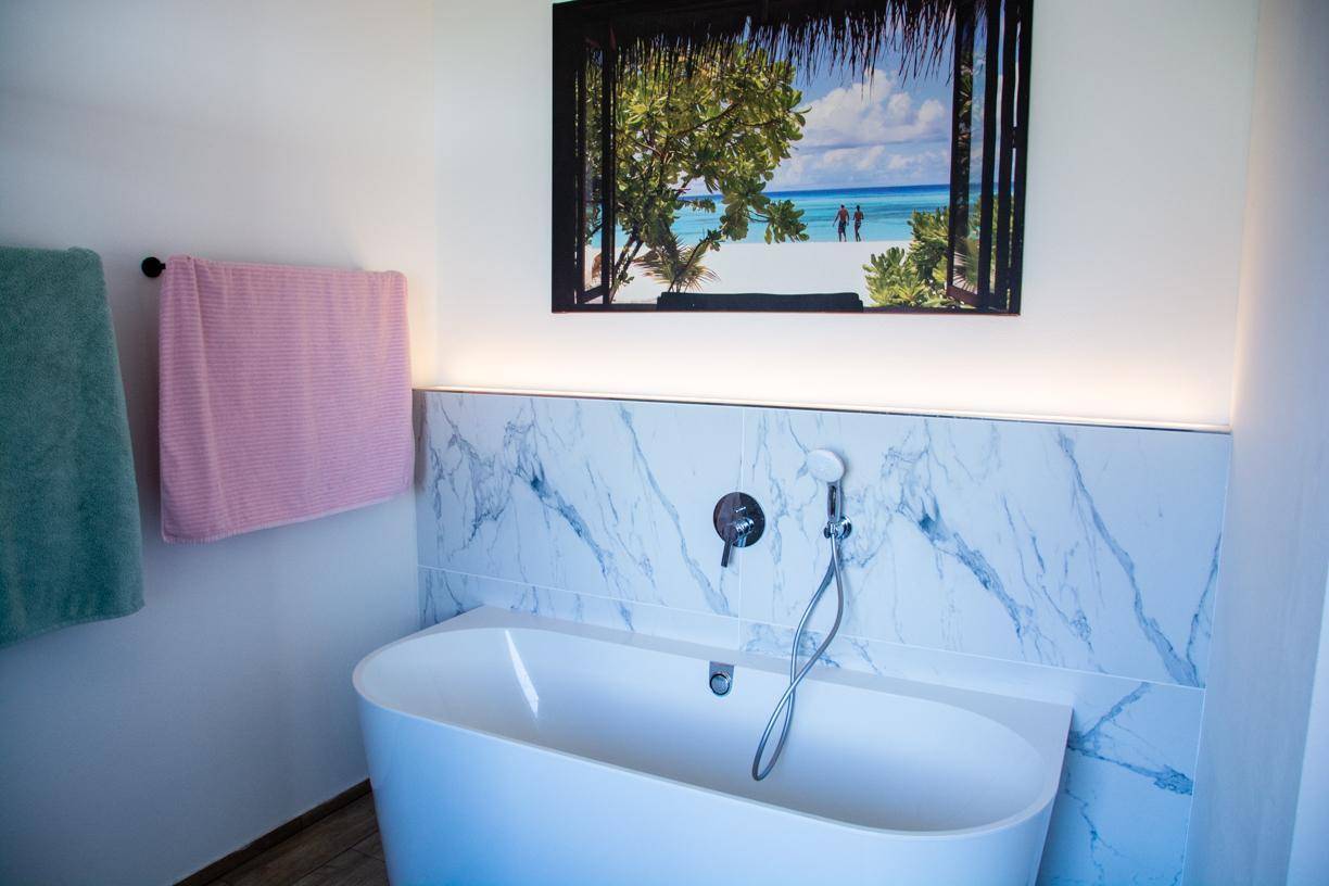 Freistehende Badewanne in einem modernen Badezimmer mit Marmoroptik-Fliesen und Handbrause.