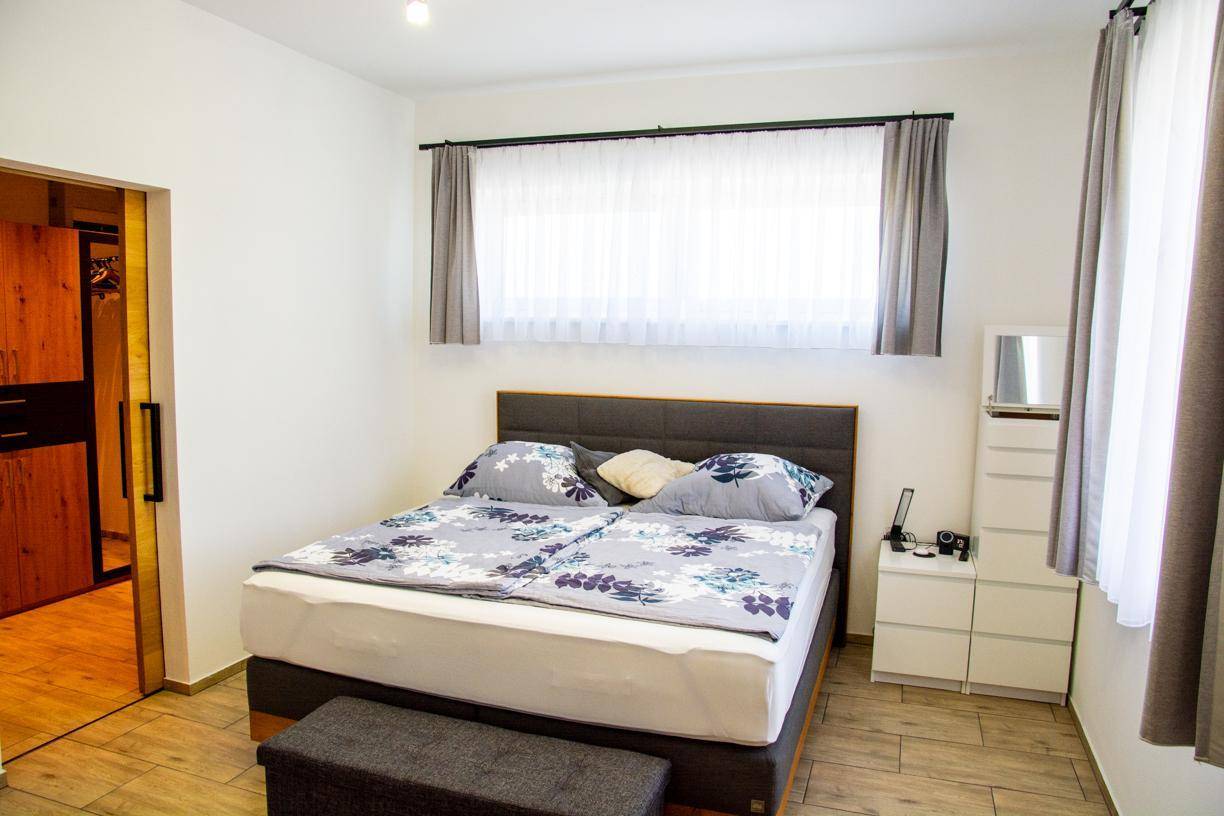 Helles Schlafzimmer mit Doppelbett, Nachttisch und großem Fenster.