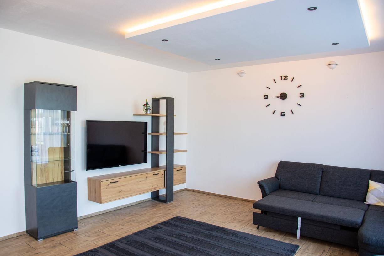 Gemütliches Wohnzimmer mit dunklem Sofa, moderner Wohnwand und stilvoller Wanduhr an der weißen Wand.