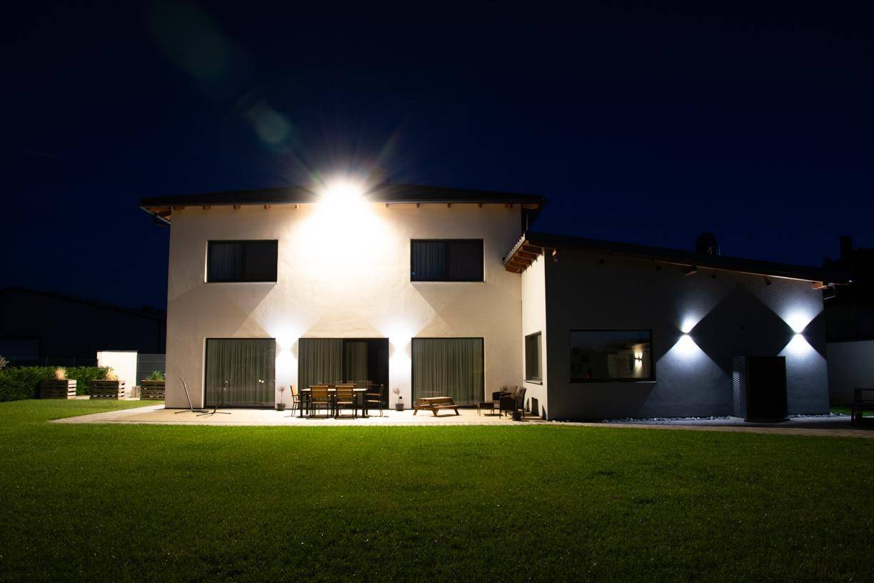 Hinterhof mit großer Rasenfläche und möblierter Terrasse, beleuchtet bei Nacht.
