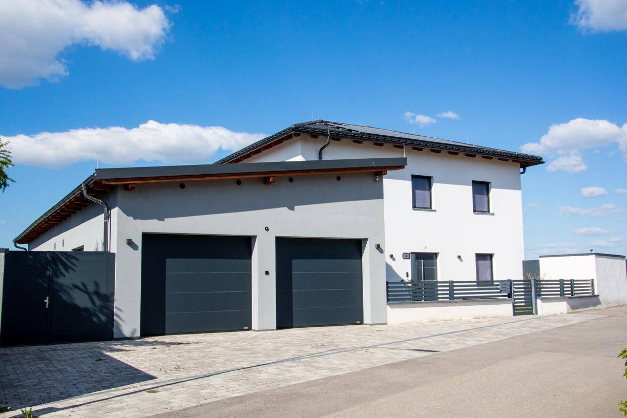 Seitenansicht des Hauses und der Doppelgarage mit modernen Garagentoren und Zaun.