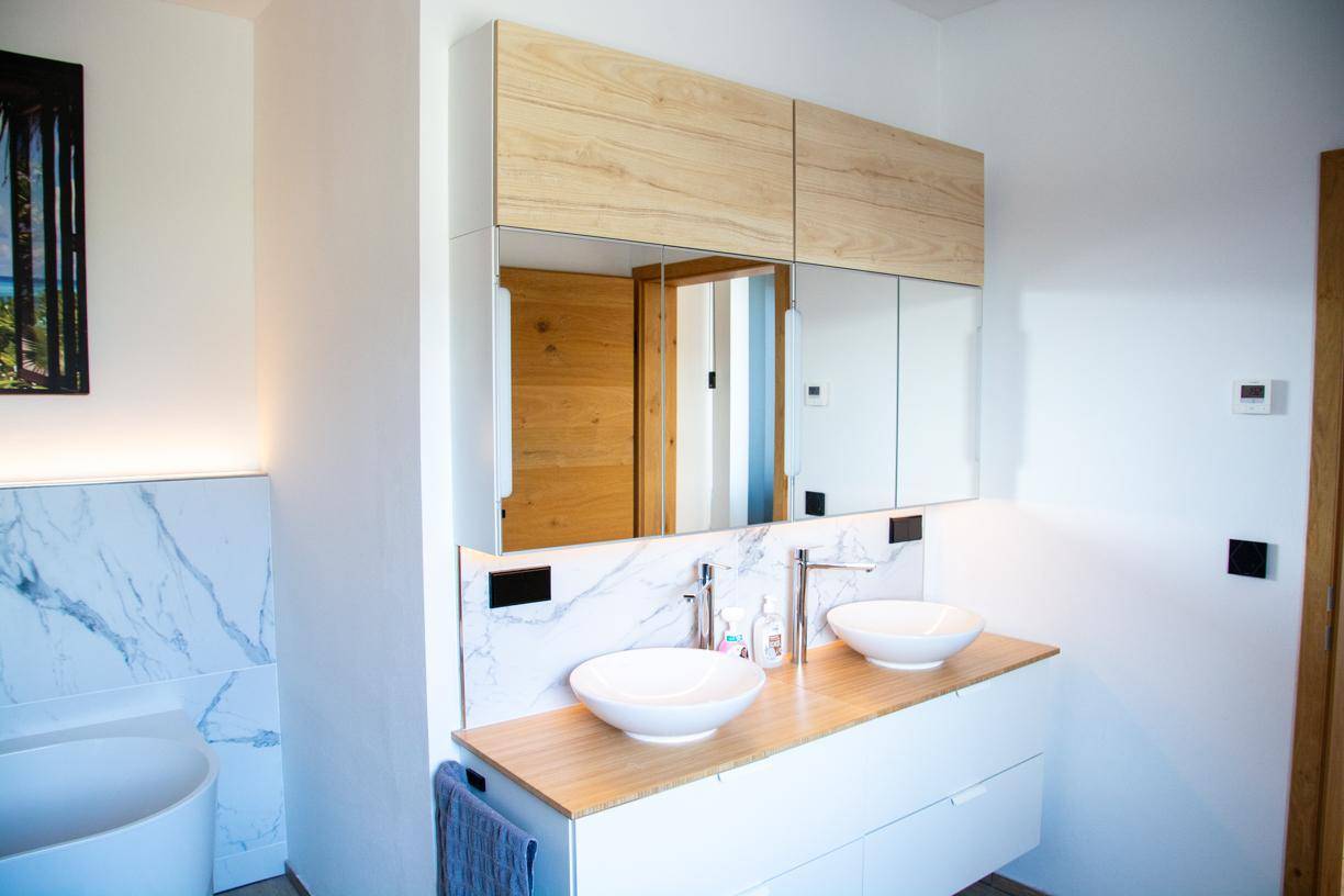 Modernes Badezimmer mit Doppelwaschbecken, Holzunterschrank und Spiegelschrank.
