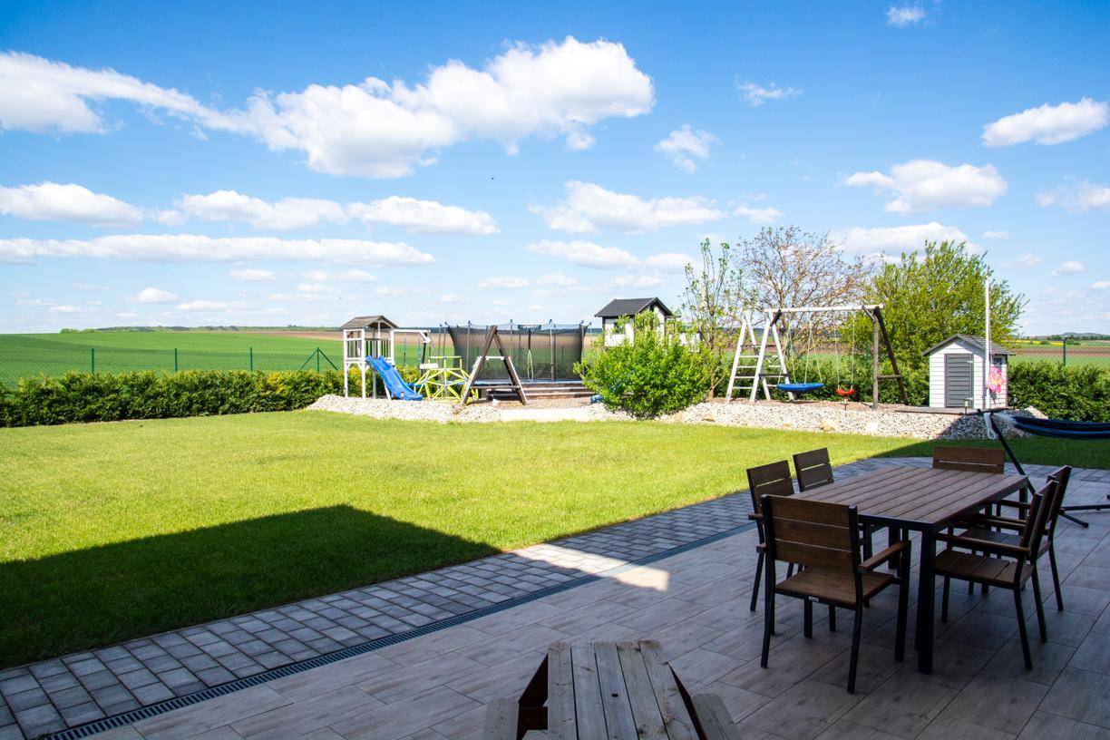 Terrasse mit Esstisch im Freien, Blick auf den Rasen, Spielplatz und weite Felder.
