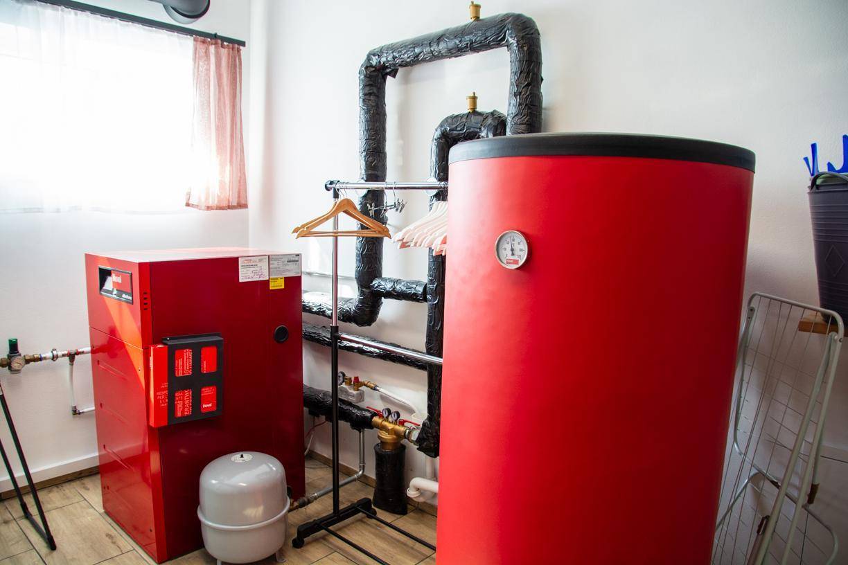 Heizsystem und großer roter Warmwasserspeicher in einem Technikraum.