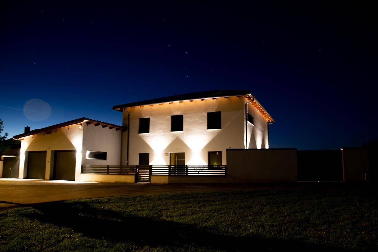 Freistehendes Einfamilienhaus bei Nacht mit beleuchteter Fassade und Vorgarten.