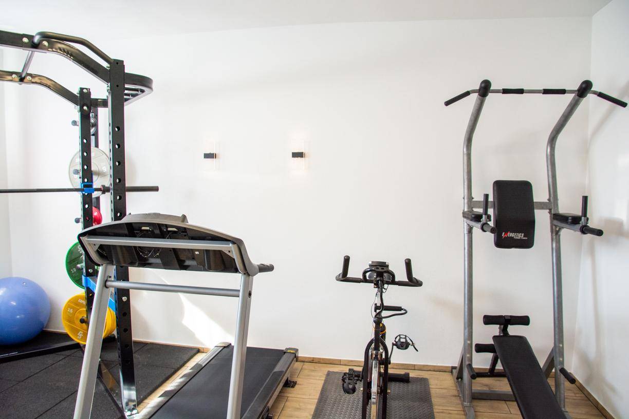 Verschiedene Fitnessgeräte wie Laufband und Hantelbank in einem hellen Raum.