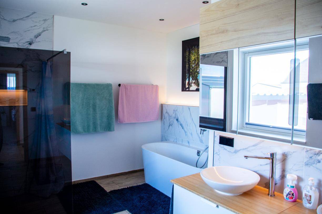 Elegantes Badezimmer mit freistehender Badewanne, modernem Waschbecken und Fenster.