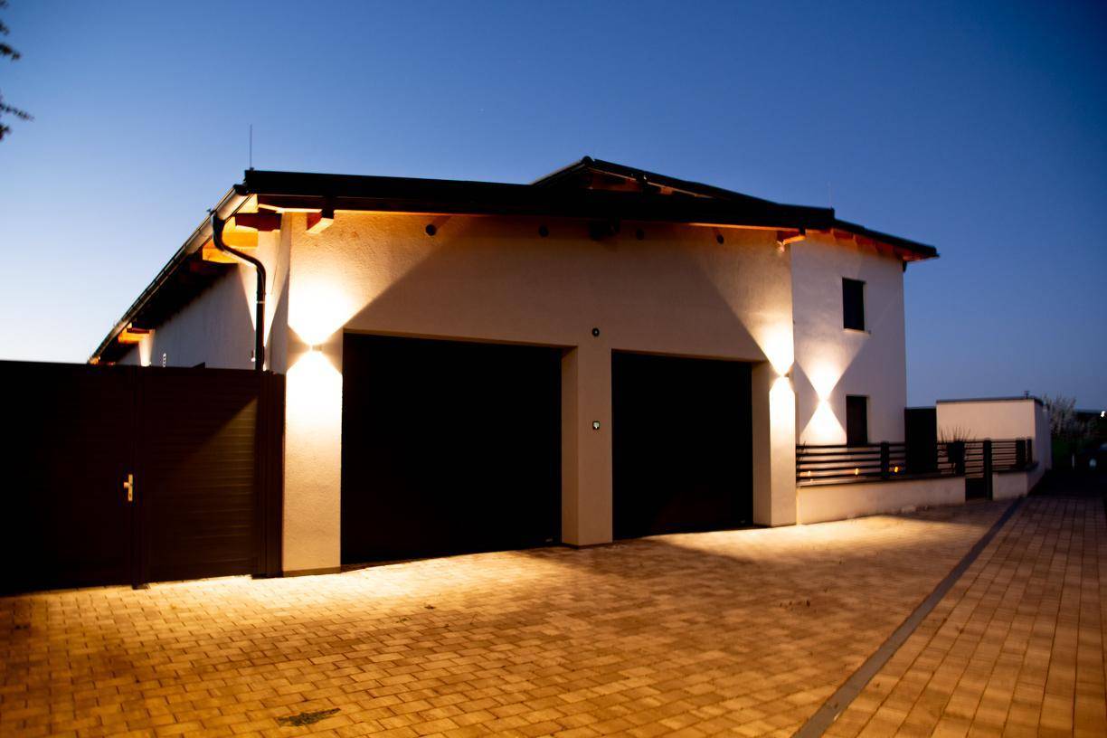 Abendaufnahme der Garage mit beleuchteter Fassade und zwei Garagentoren unter dunklem Himmel.
