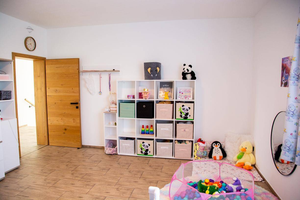 Helles Kinderzimmer mit Spielzeug, Regalen und einem bunten Spielbereich.