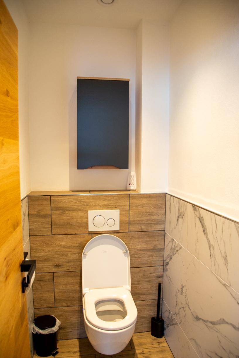 Modernes Gäste-WC mit wandhängender Toilette und Holzverkleidung.