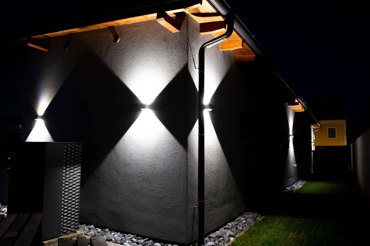 Seitenansicht des Hauses bei Nacht mit dekorativer Wandbeleuchtung und Kiesbeet.