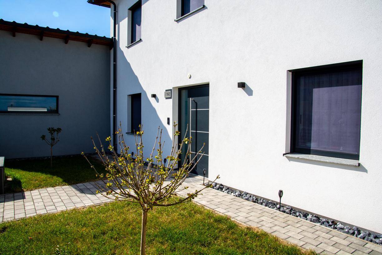Eingangsbereich des Hauses mit gepflastertem Weg, kleinem Baum und dekorativen Steinen.