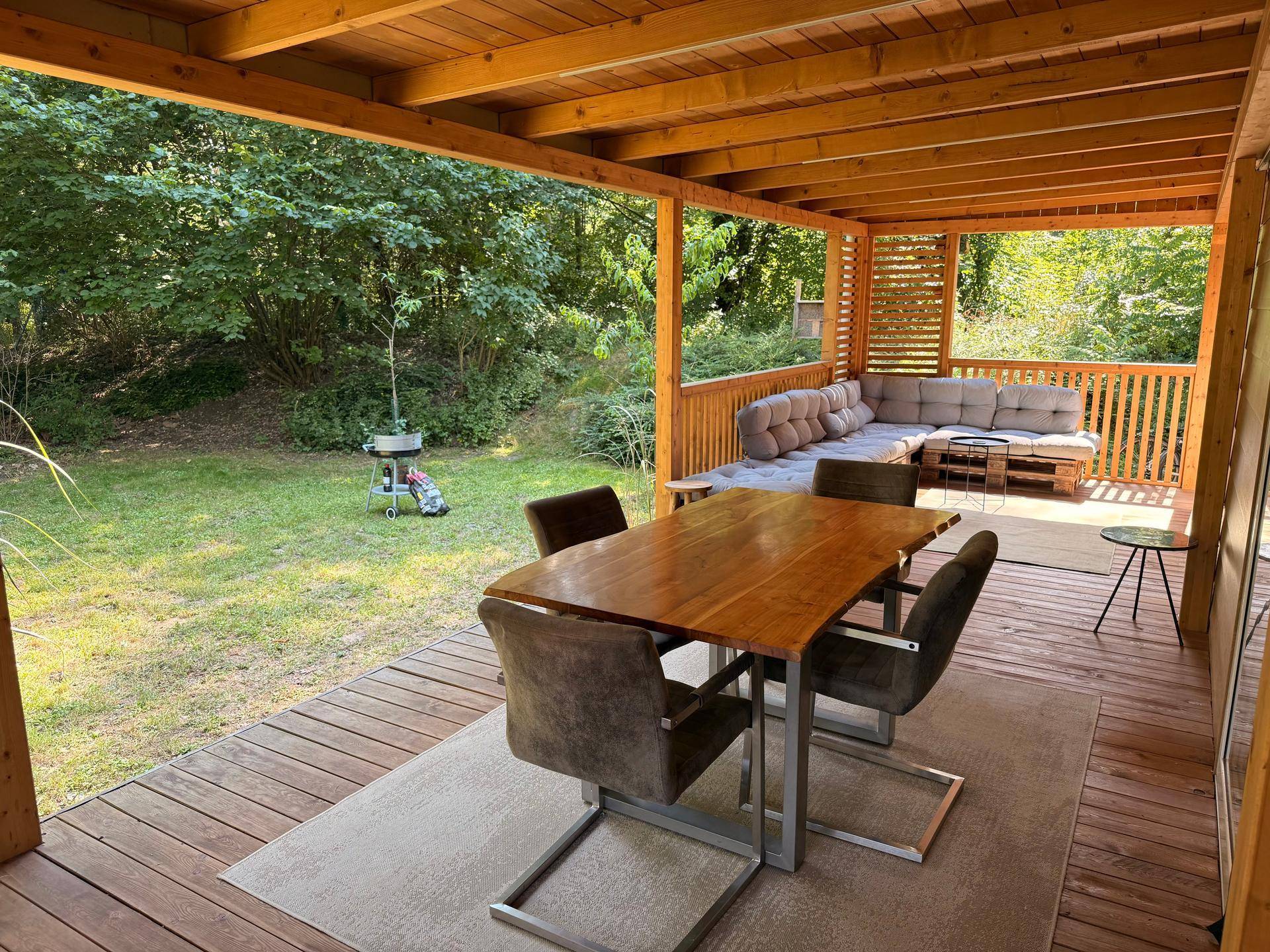 Geräumige überdachte Holzterrasse mit Esstisch, Lounge-Bereich und Blick ins Grüne.