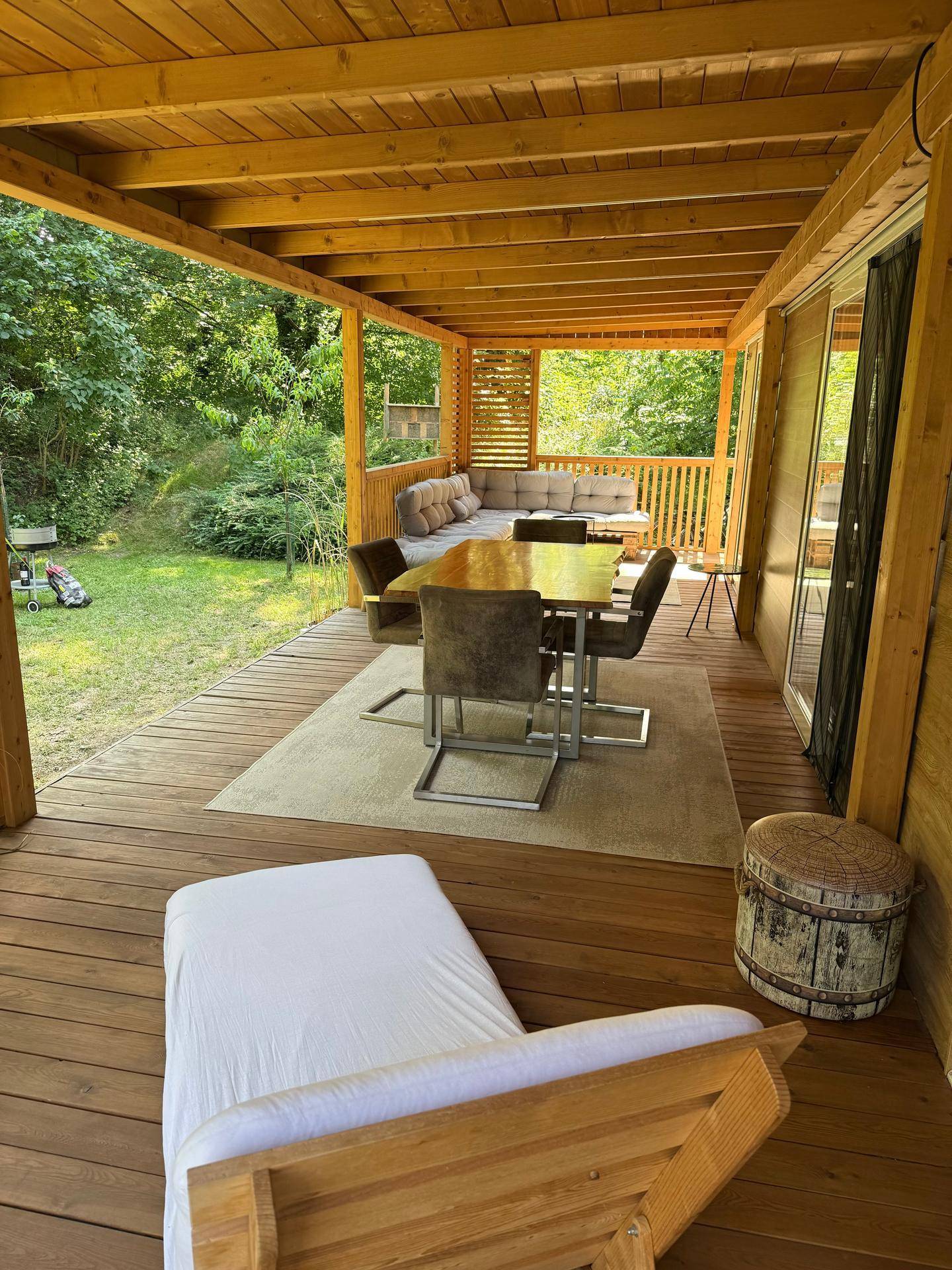 Helle überdachte Terrasse mit Essbereich, Liegestuhl und weitem Blick in den grünen Garten.