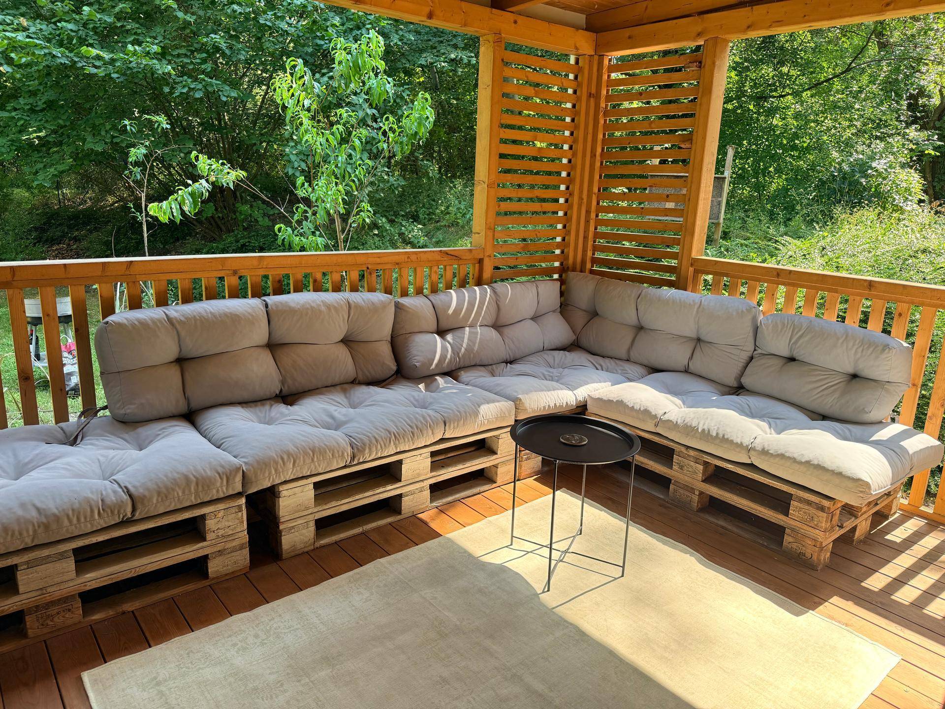 Gemütlicher Lounge-Bereich auf der überdachten Terrasse mit Palettenmöbeln und bequemen Kissen.