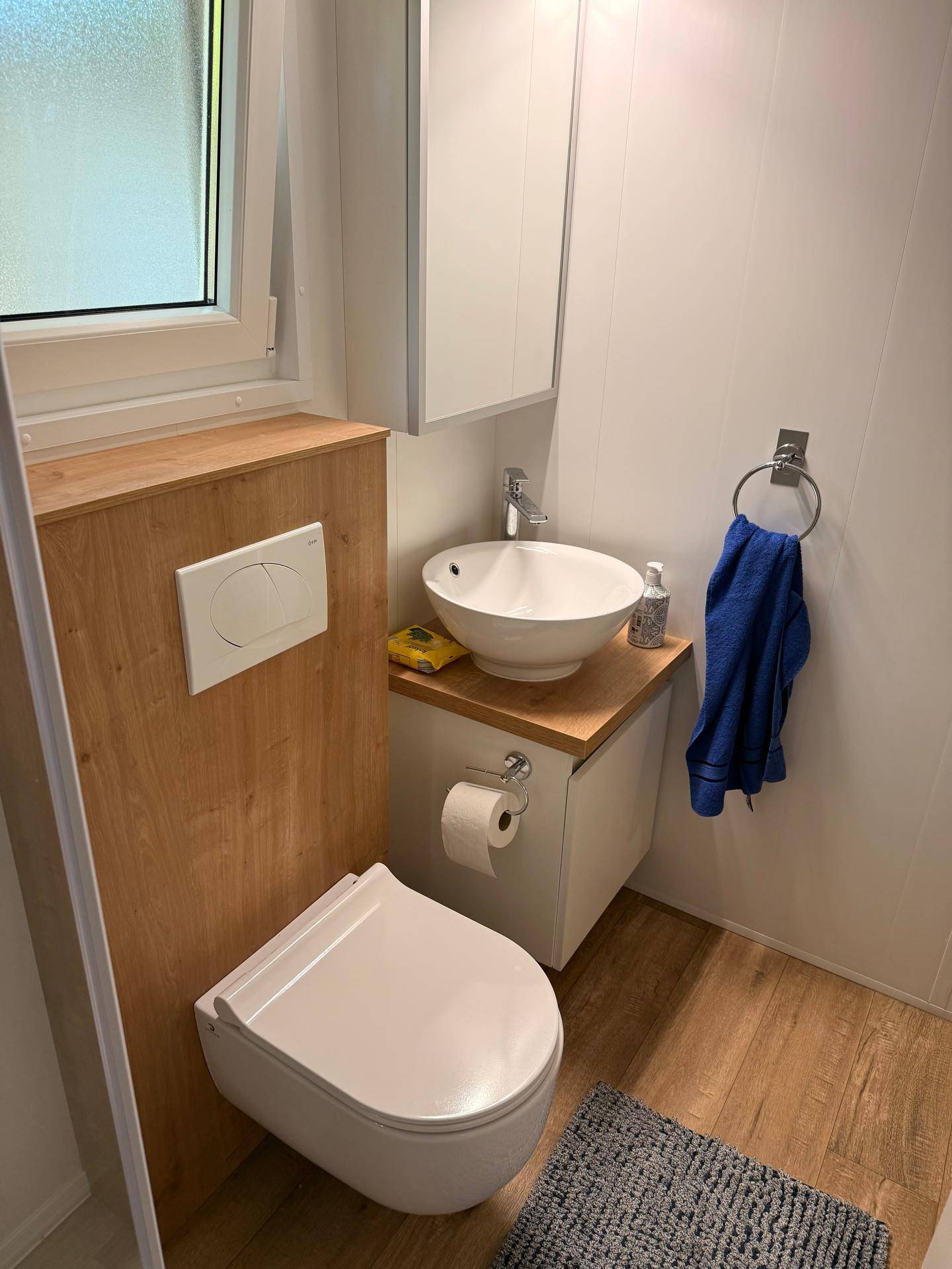 Kleines WC mit wandhängender Toilette, modernem Aufsatzwaschbecken und Fenster für Tageslicht.