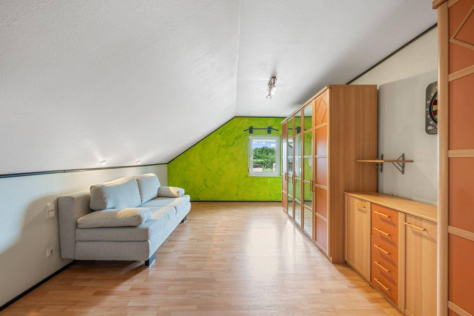 Dachgeschosszimmer mit Sofa, Kleiderschrank und leuchtend grüner Akzentwand.