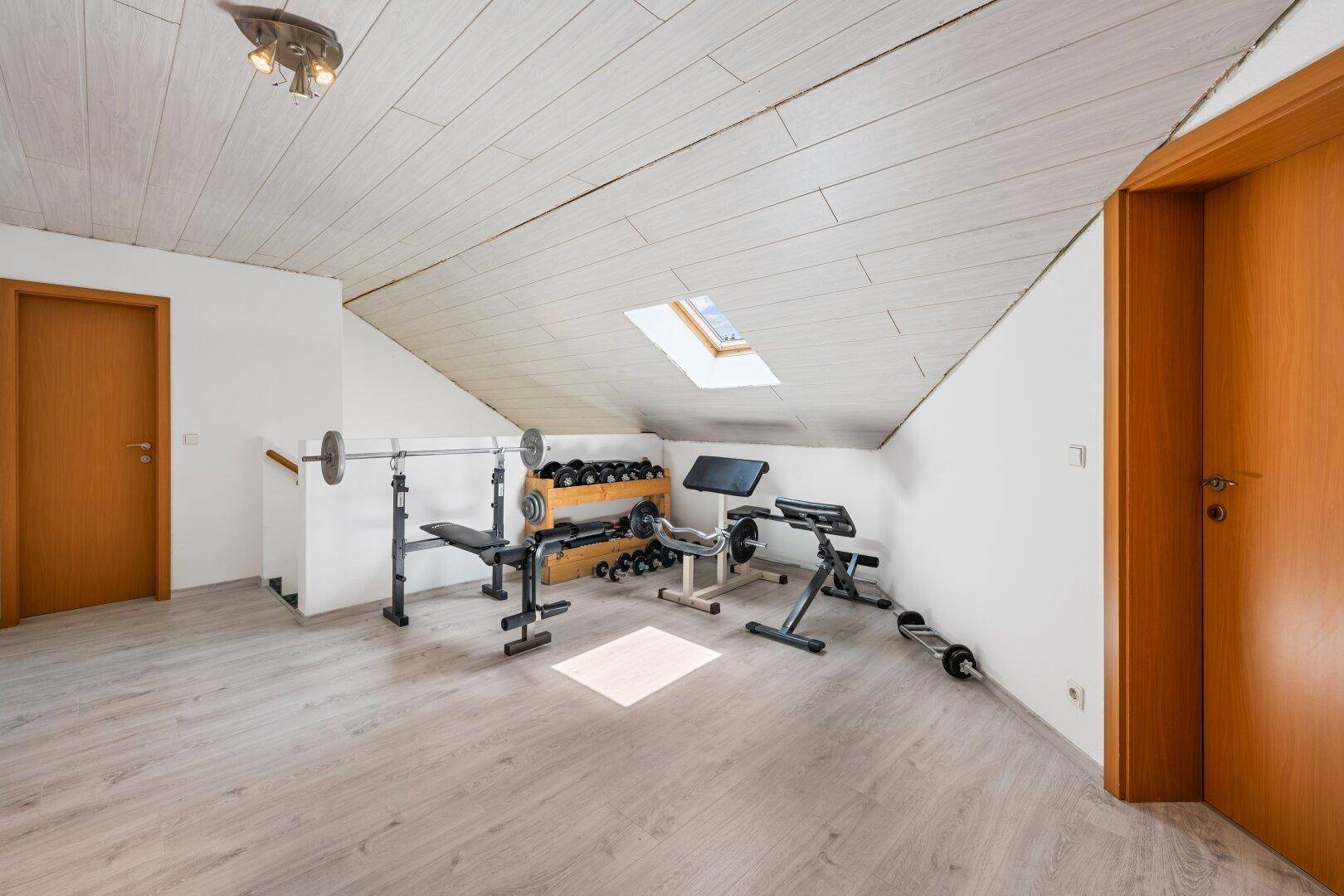 Dachgeschoss-Fitnessraum mit Trainingsgeräten, Schrägdach und Dachfenster.