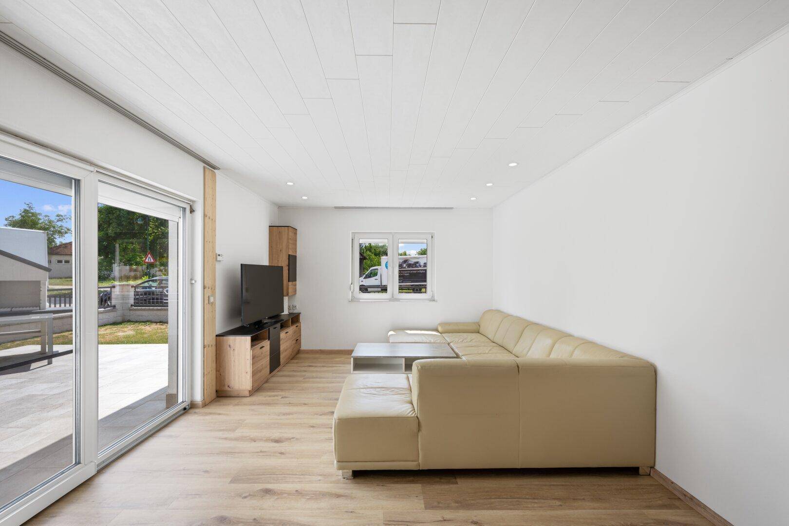 Helles Wohnzimmer mit beigem Sofa, Holzboden und Zugang zur Terrasse.