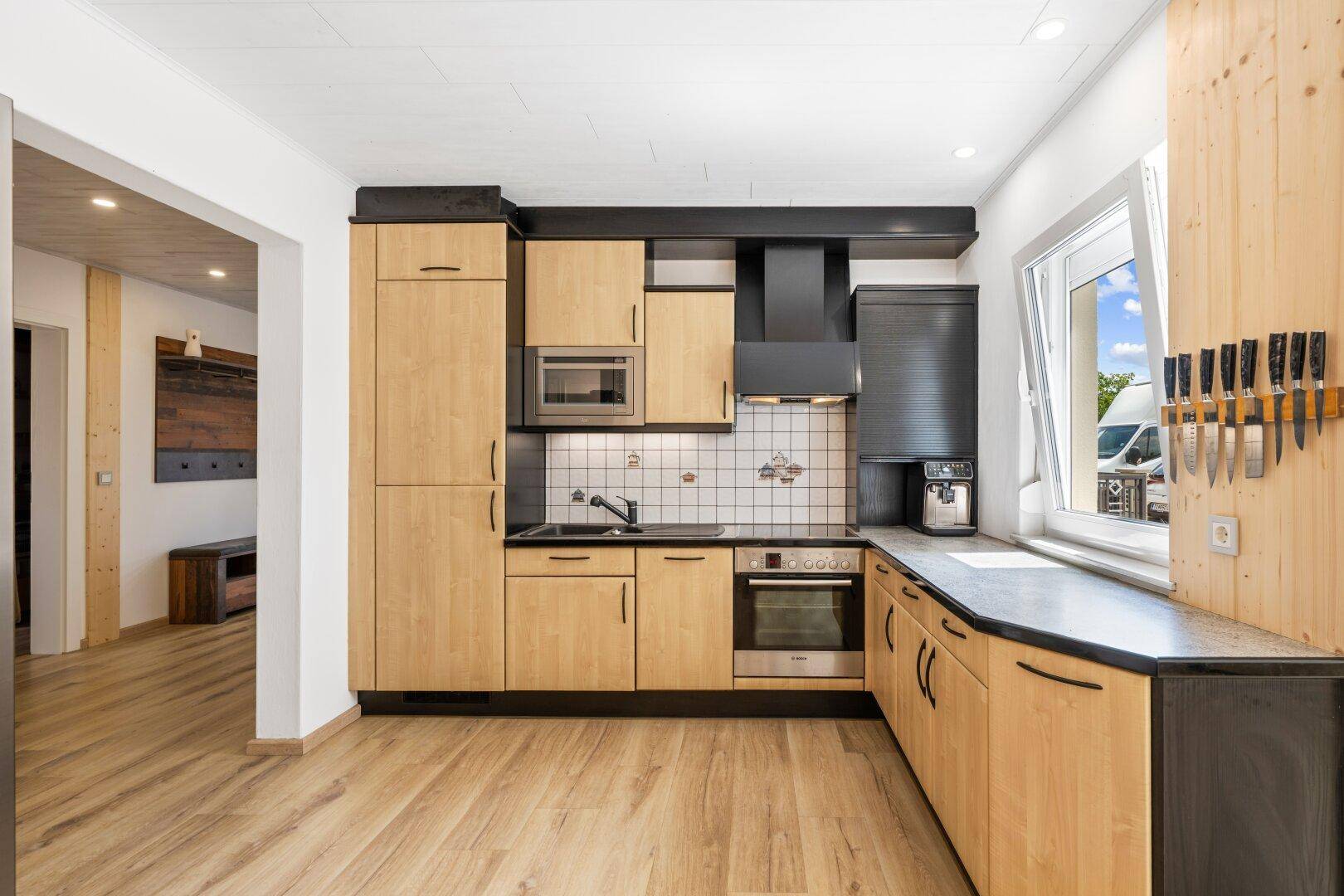 Funktionale Küche mit hellen Holzschränken, schwarzen Arbeitsplatten und Fenster.