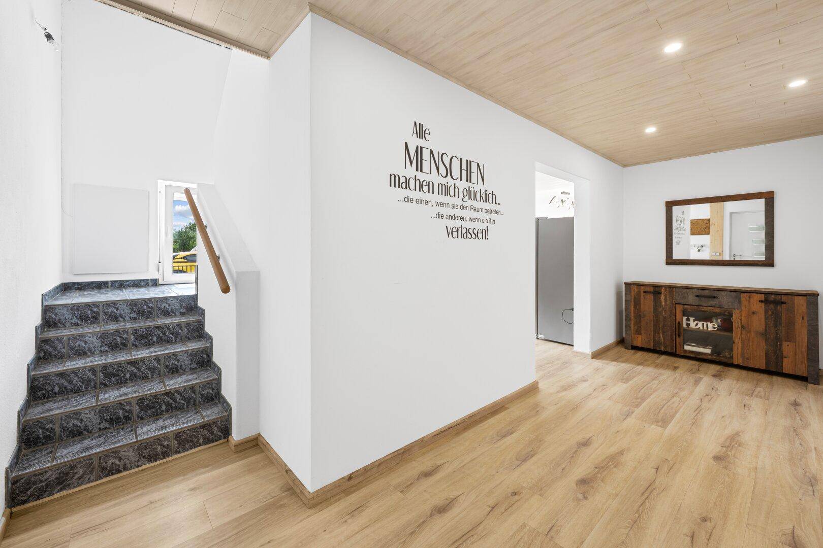 Heller Flur mit Laminatboden, Treppe und dekorativer Wandbeschriftung.