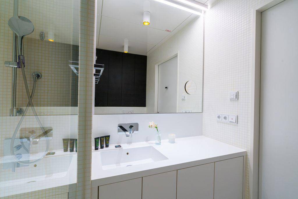 Modernes Badezimmer mit integriertem Waschbecken, großem Spiegel und Duschbereich mit Mosaikfliesen.