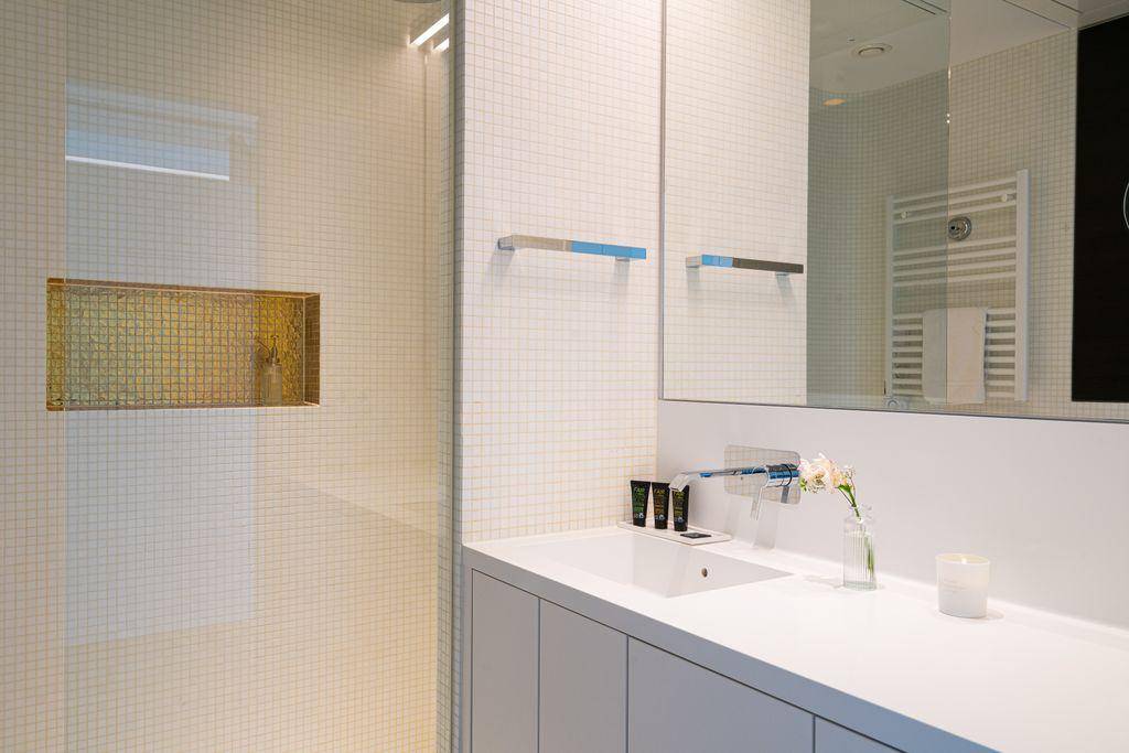 Helles Badezimmer mit modernem Waschbecken, großem Spiegel und einer Duschkabine mit Mosaikfliesen.