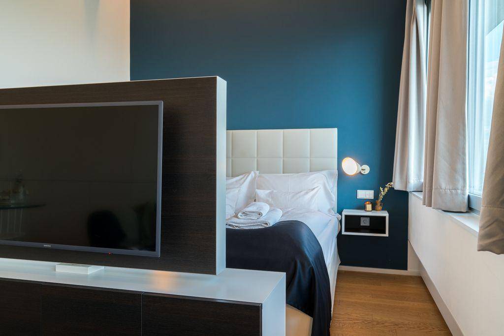 Schlafzimmer mit großem Fernseher, blauer Akzentwand und bequemen Bett.