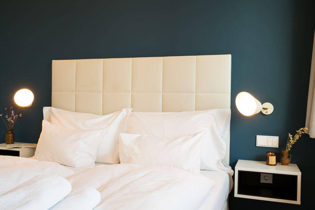 Gemütliches Schlafzimmer mit gepolstertem Kopfteil, blauer Wand und Nachttischen mit Beleuchtung.