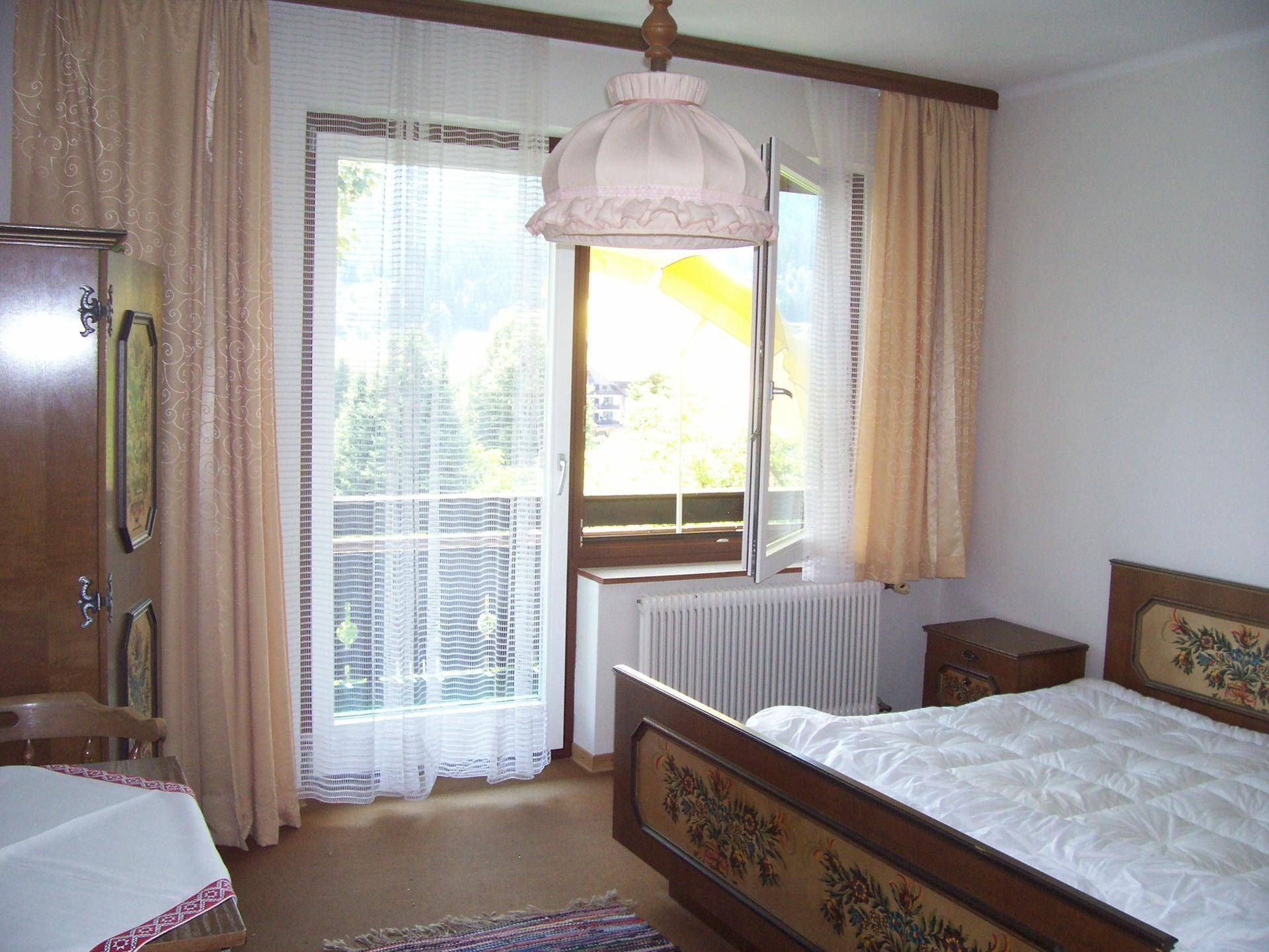 Helles Schlafzimmer mit traditionellem Holzbett, Fenster und Blick ins Grüne.