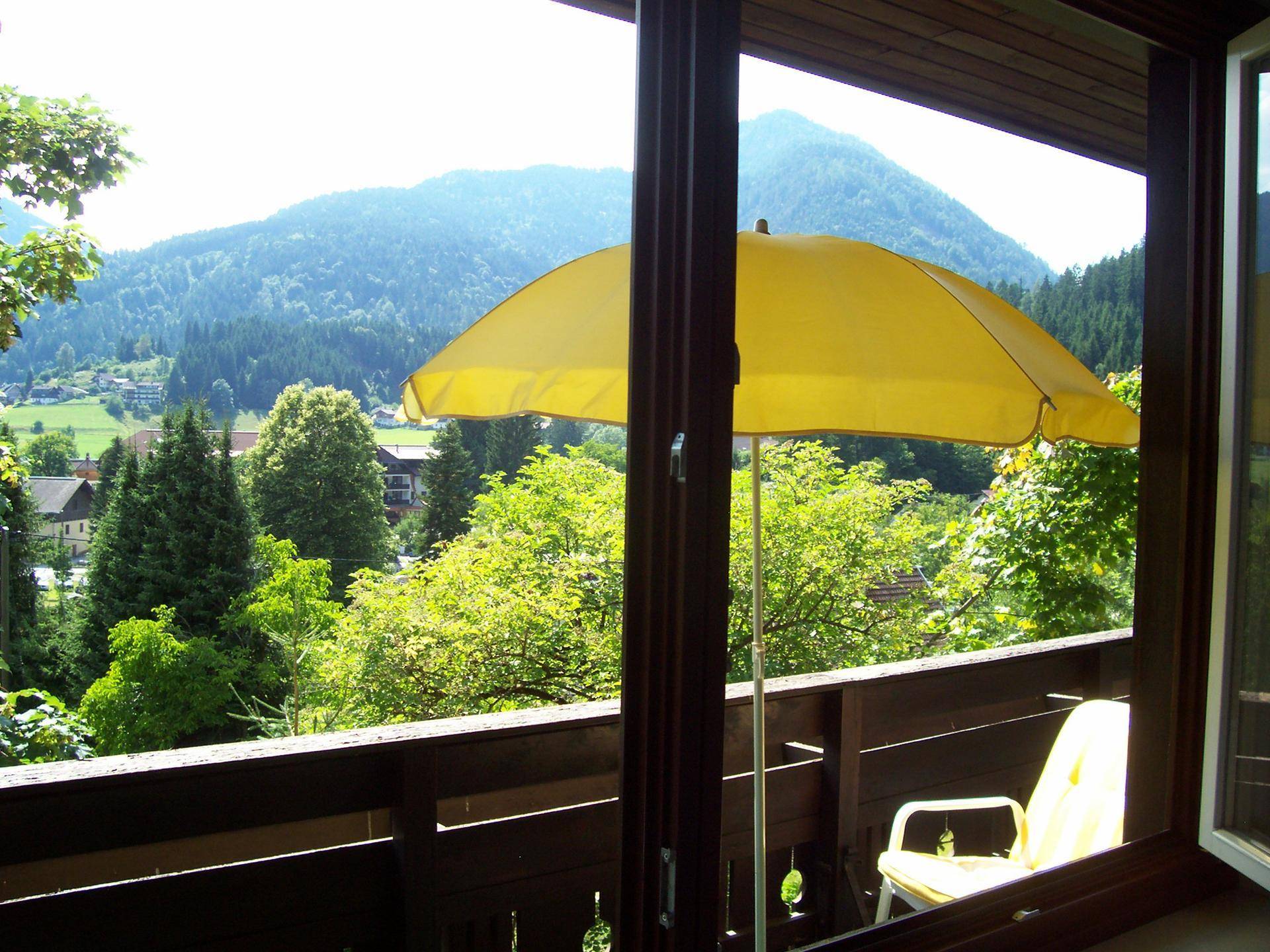 Balkon mit gelbem Sonnenschirm und weitem Blick auf die umliegende Berglandschaft und das Tal.