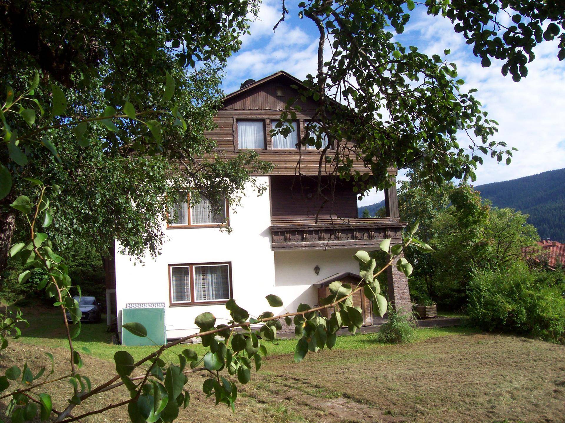 Charmantes Haus mit weißer Fassade und Holzbalkonen, umgeben von üppiger grüner Vegetation.