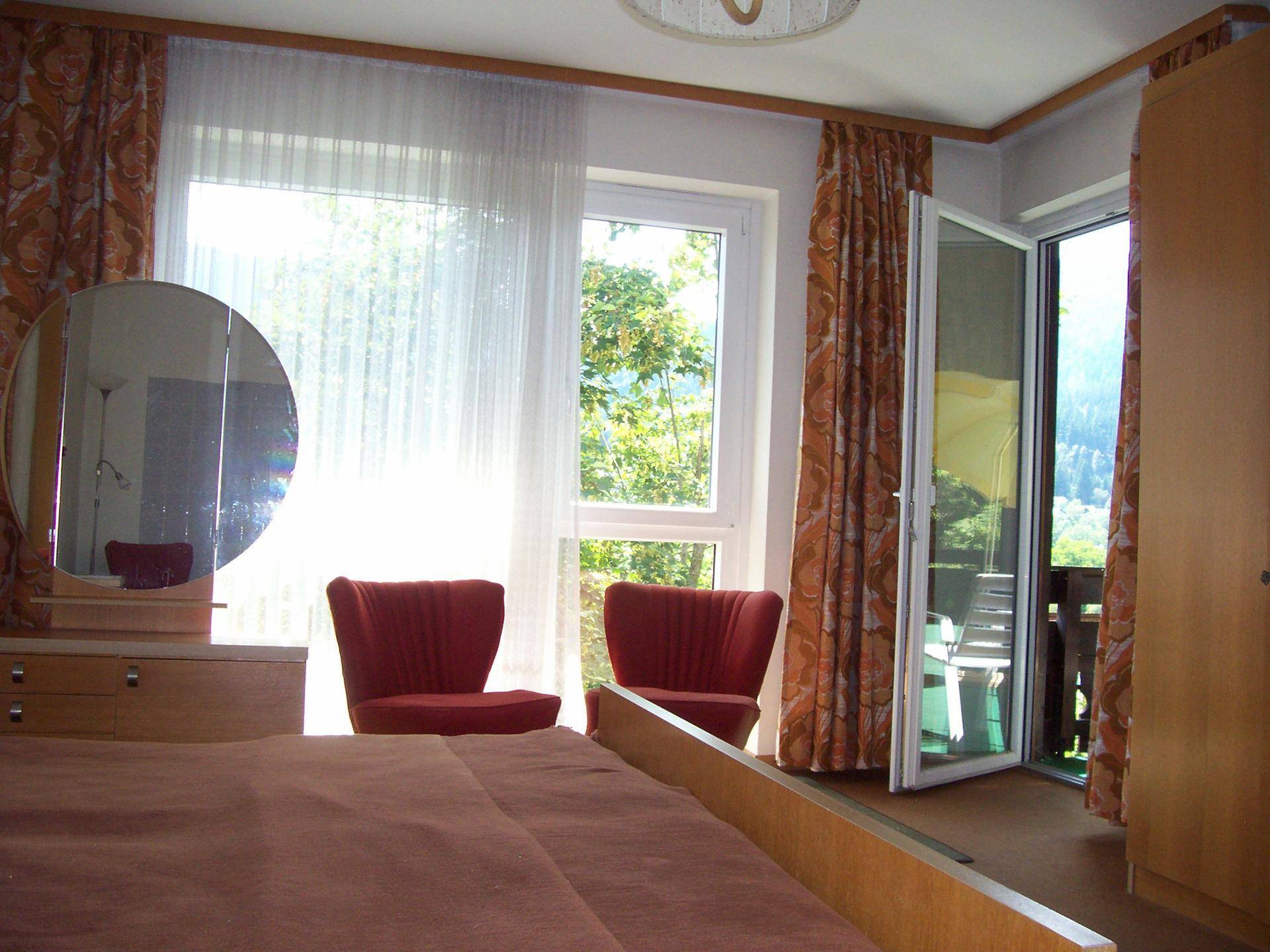 Schlafzimmer mit Doppelbett, Schminktisch und Zugang zu einem Balkon mit Bergblick.