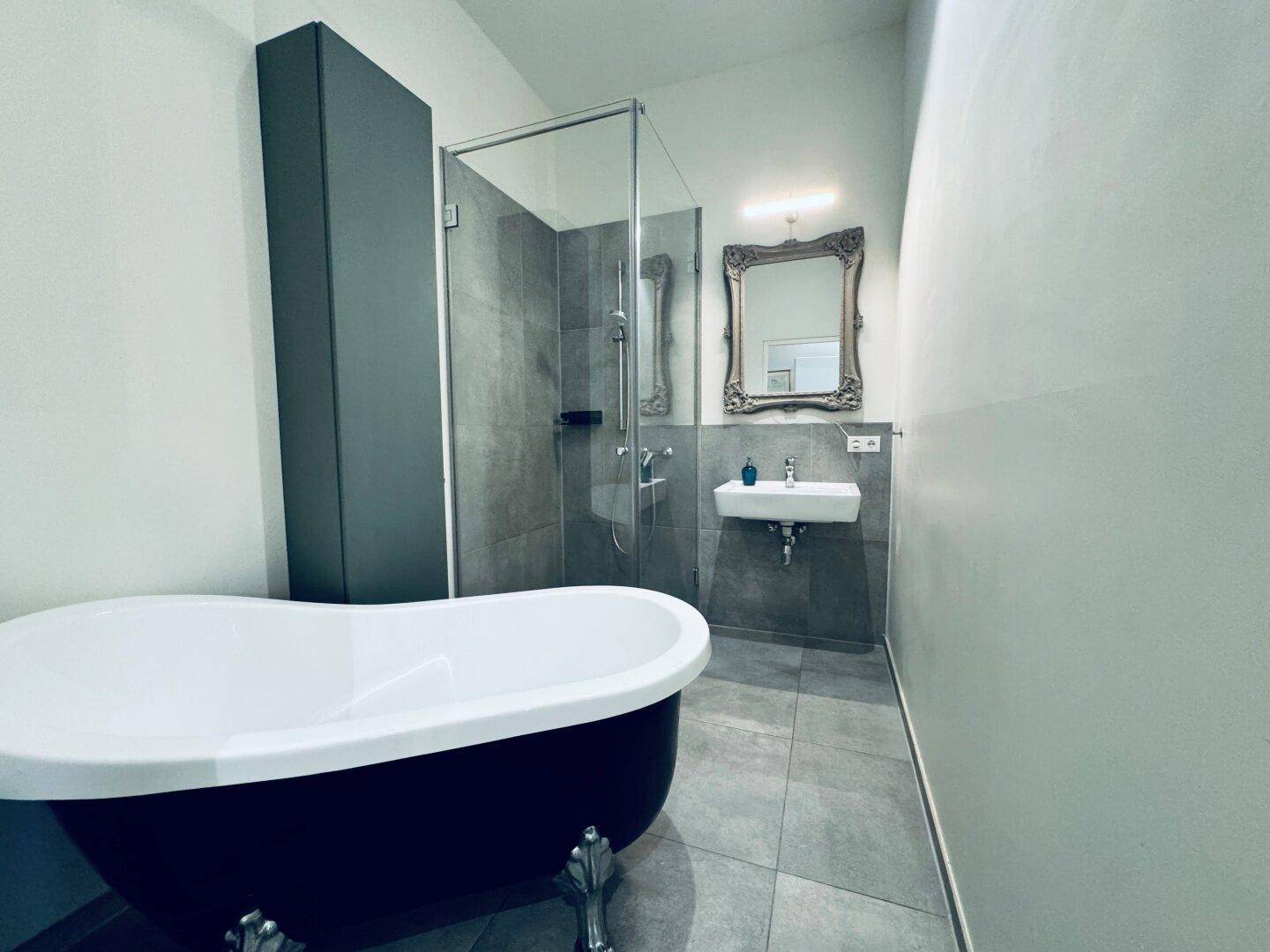 Modernes Badezimmer mit freistehender Badewanne, Glasdusche und eleganten Grautönen.