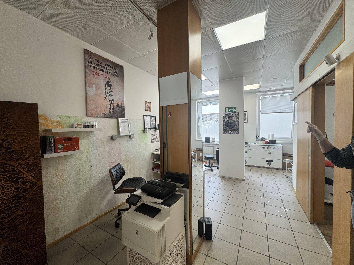 Empfangsbereich mit einem Drucker, einem großen Spiegel und Zugang zu weiteren Geschäftsräumen.