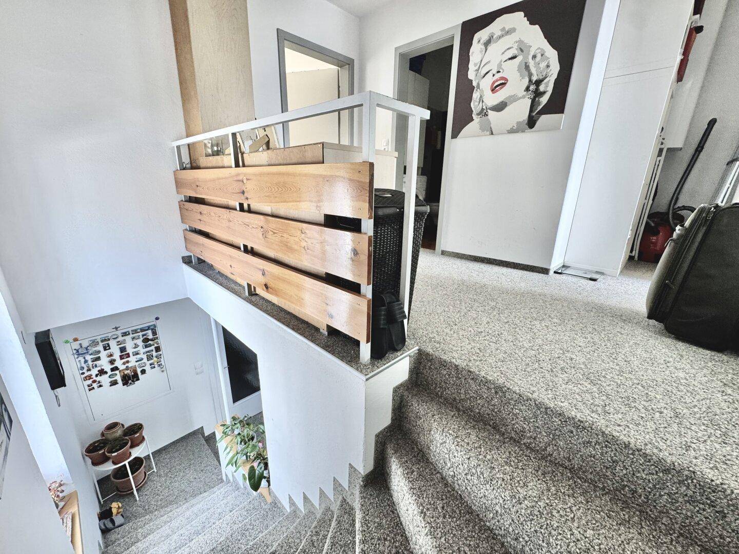 Treppenhaus mit Teppichboden und einem modernen Holzgeländer, das zu den oberen Etagen führt.