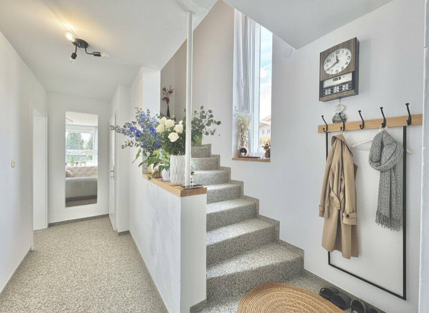 Heller Flur mit Treppe, Teppichboden und einem hohen Fenster, das viel Licht hereinlässt.