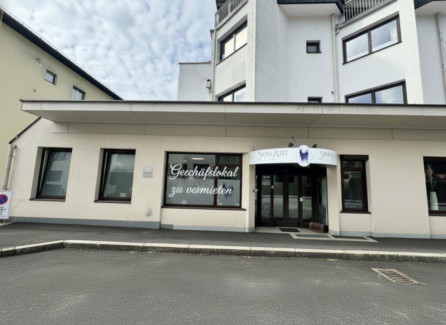 Außenansicht eines gepflegten Geschäftsgebäudes mit großen Fenstern und einem Parkplatz davor.