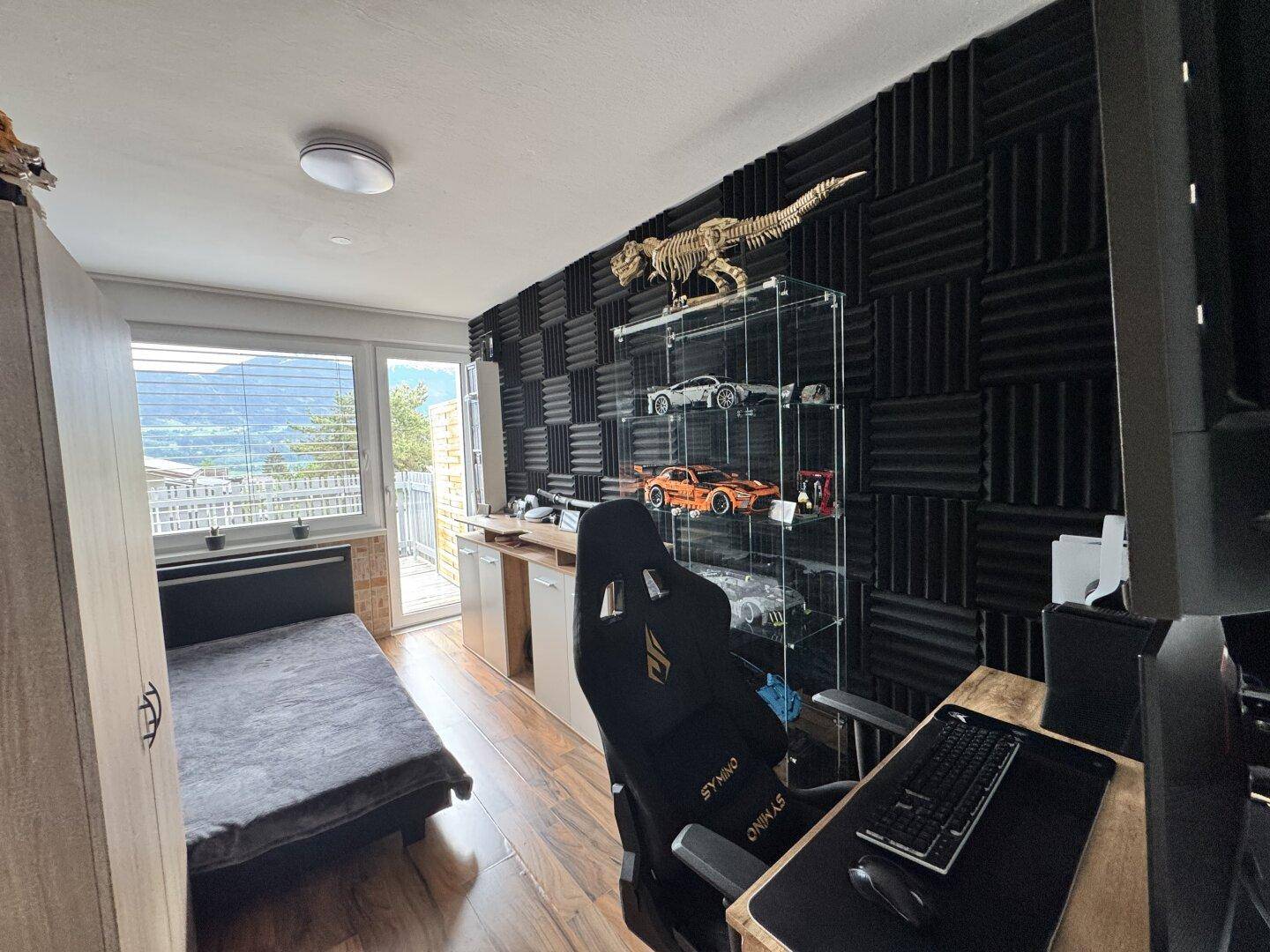 Schlafzimmer mit Holzboden, Schreibtisch und einer Wand mit Schalldämmplatten.
