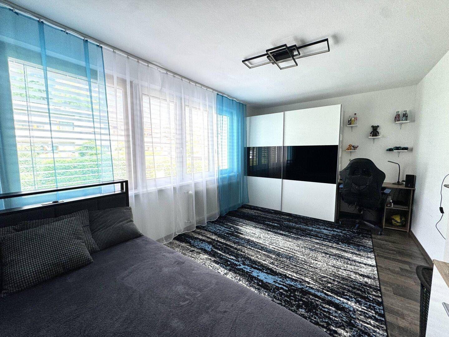 Helles Schlafzimmer mit großem Fenster, Teppich und einem modernen Kleiderschrank.
