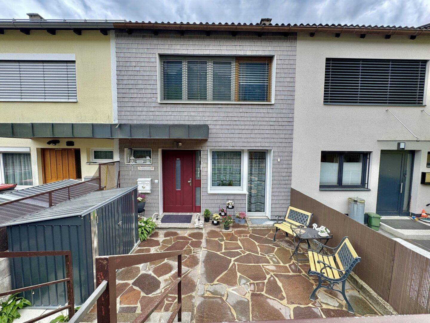 Eingangsbereich mit gepflastertem Patio, Sitzgelegenheiten und einem kleinen Schuppen neben dem Haus.