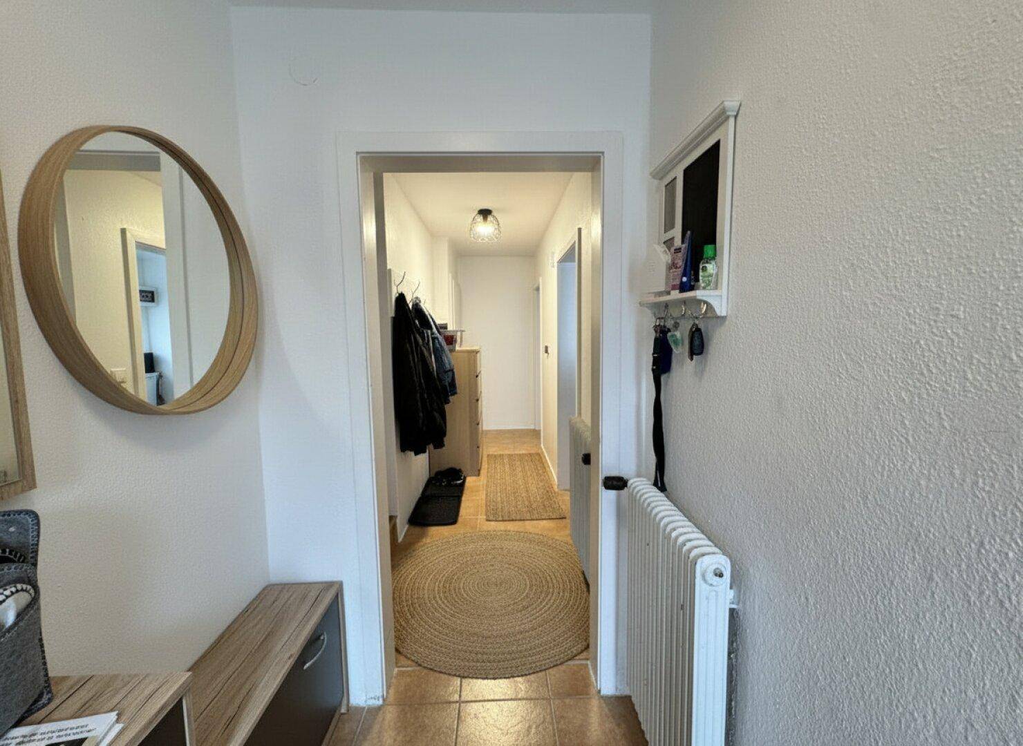 Heller Flur mit Fliesenboden, einem runden Spiegel und Zugang zu weiteren Räumen.